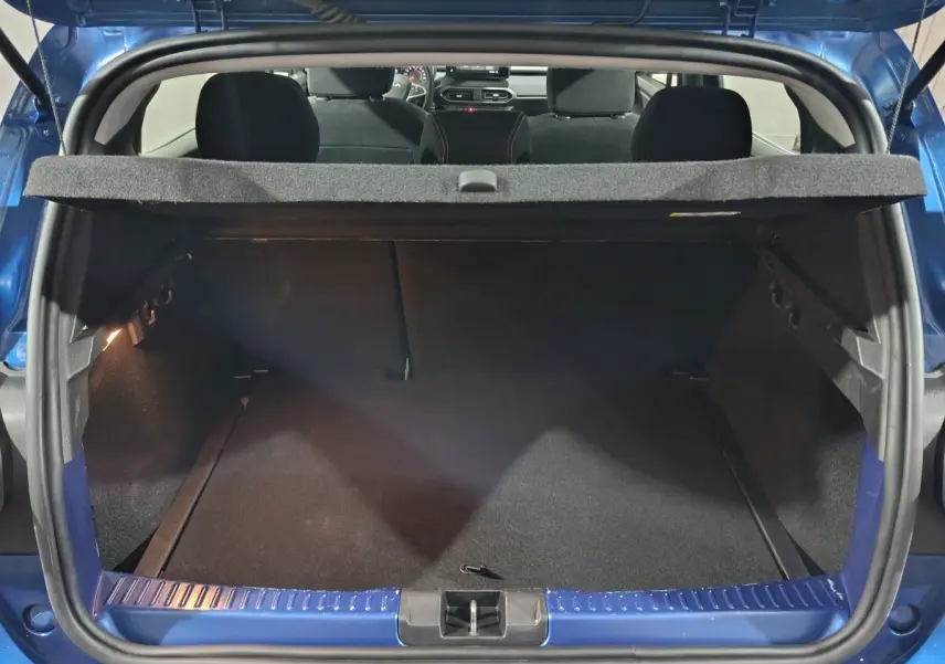 Coffre ouvert vu de l'arrière d'une Dacia Sandero Extreme+ TCe 110 bleu 2024, intérieur noir et tablette de coffre visible.
