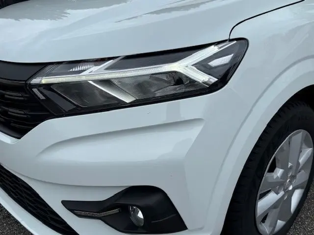Gros plan sur le phare avant droit blanc glacier du Dacia Sandero 2023 avec détails LED et partie de la calandre noire.