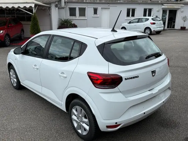 Vue 3/4 arrière droite d'une Dacia Sandero blanche glacier 2023, avec feux arrière rouges et antenne de toit noire.