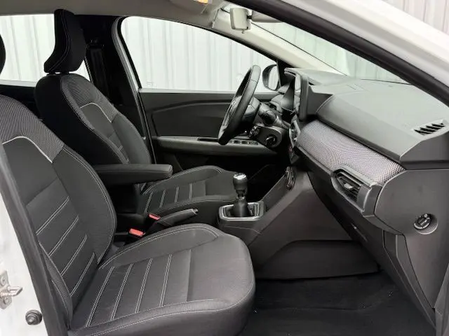 Intérieur avant de la Dacia Sandero blanche 2023, vue côté conducteur, sièges noirs et tableau de bord moderne.