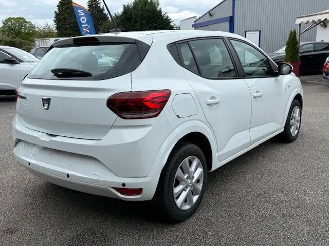 Vue 3/4 arrière droite d'une Dacia Sandero blanche glacier 2023, compacte avec feux arrière rouges et jantes argentées.