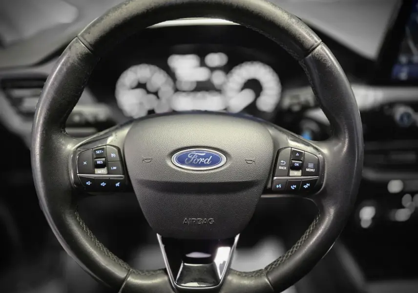 Vue rapprochée du volant noir du Ford Kuga 1.5 EcoBlue 2020 avec commandes intégrées et logo Ford central.