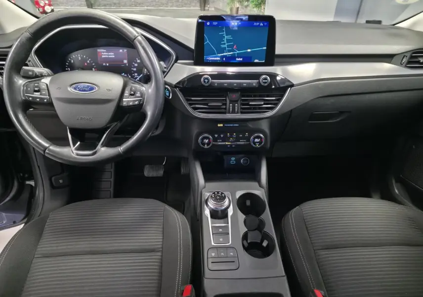 Vue intérieure avant du Ford Kuga 2020 gris, avec volant multifonction, écran tactile central et console avec sélecteur rotatif.