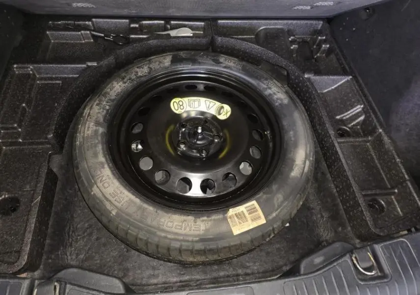 Gros plan sur la roue de secours galette noire 17 pouces dans le coffre du Ford Kuga gris 2020.