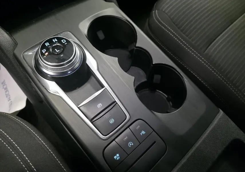 Vue rapprochée de la console centrale noire du Ford Kuga 2020 avec sélecteur rotatif de boîte auto et porte-gobelets.