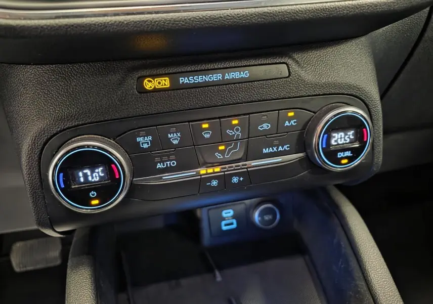Gros plan sur la console centrale noire du Ford Kuga 2020, affichant la climatisation automatique bi-zone et l'indicateur airbag passager.