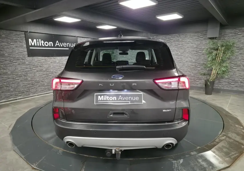 Vue arrière d'un Ford Kuga gris métallisé 2020 avec attelage fixe et feux arrière LED allumés dans un showroom.