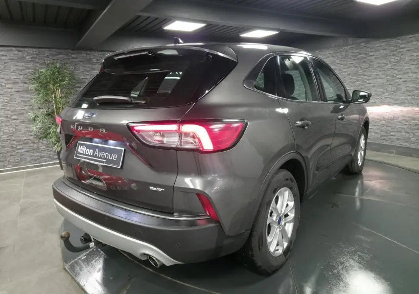 Vue 3/4 arrière droite d'un Ford Kuga gris métallisé 2020 avec attelage fixe et feux arrière LED allumés.