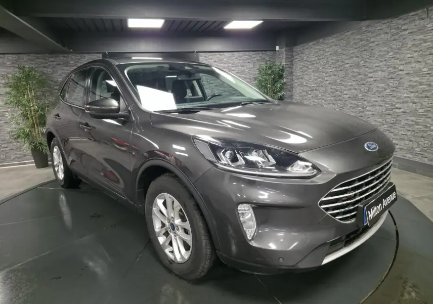 Ford Kuga gris métallisé en 3/4 avant droit avec calandre chromée et jantes alliage 17 pouces dans un showroom.