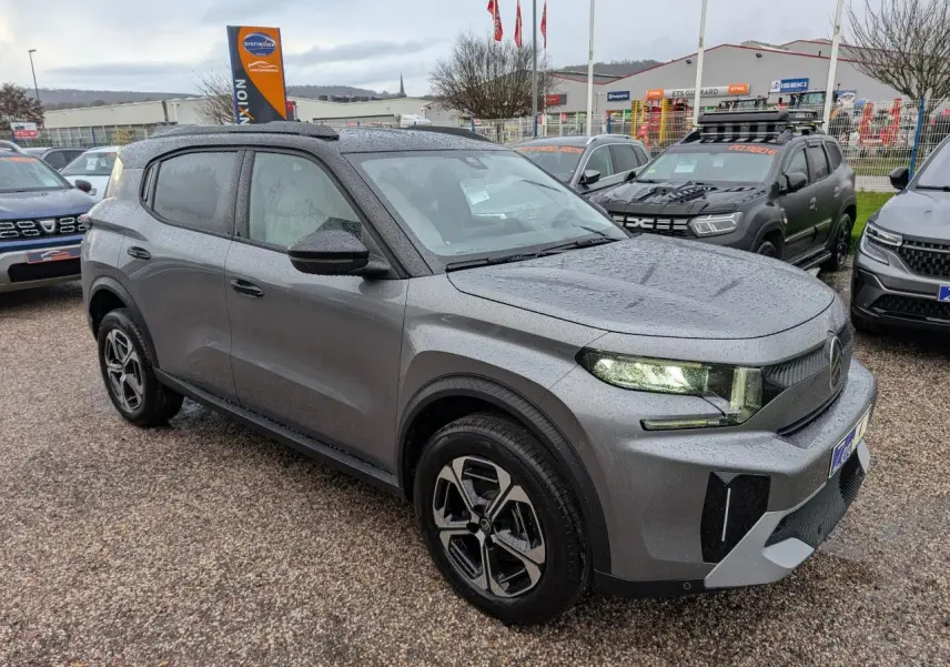 Citroën C3 Aircross 2025 gris métallisé vue 3/4 avant sous la pluie avec toit noir et jantes diamantées.