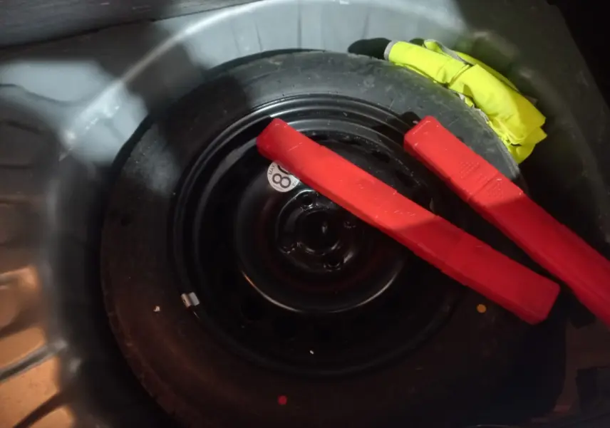 Gros plan sur la roue de secours galette noire dans le coffre d'une Dacia Sandero 2024 avec deux triangles de signalisation rouges.