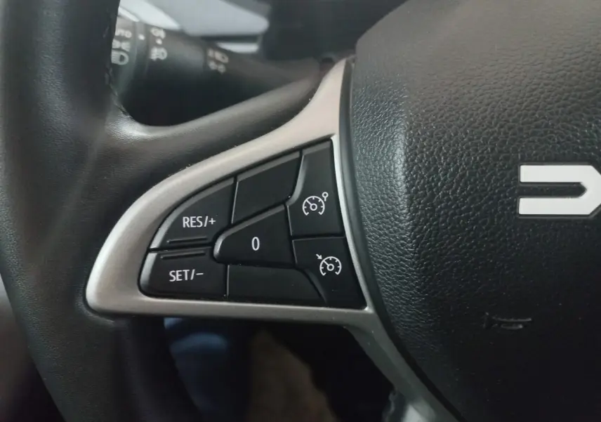 Gros plan sur les commandes de régulateur de vitesse au volant en cuir synthétique noir de la Dacia Sandero 2024.