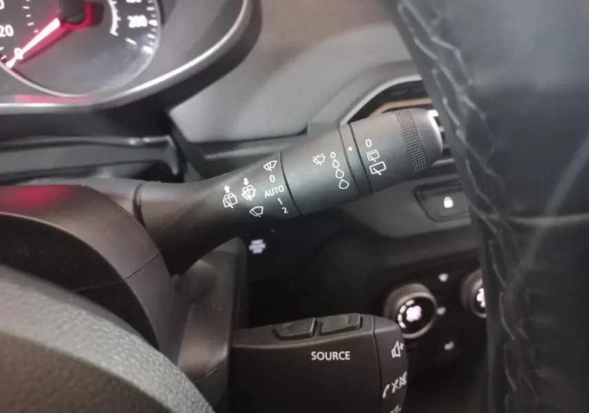 Gros plan sur la commande des essuie-glaces à gauche du volant cuir noir dans le tableau de bord d’une Dacia Sandero verte 2024.