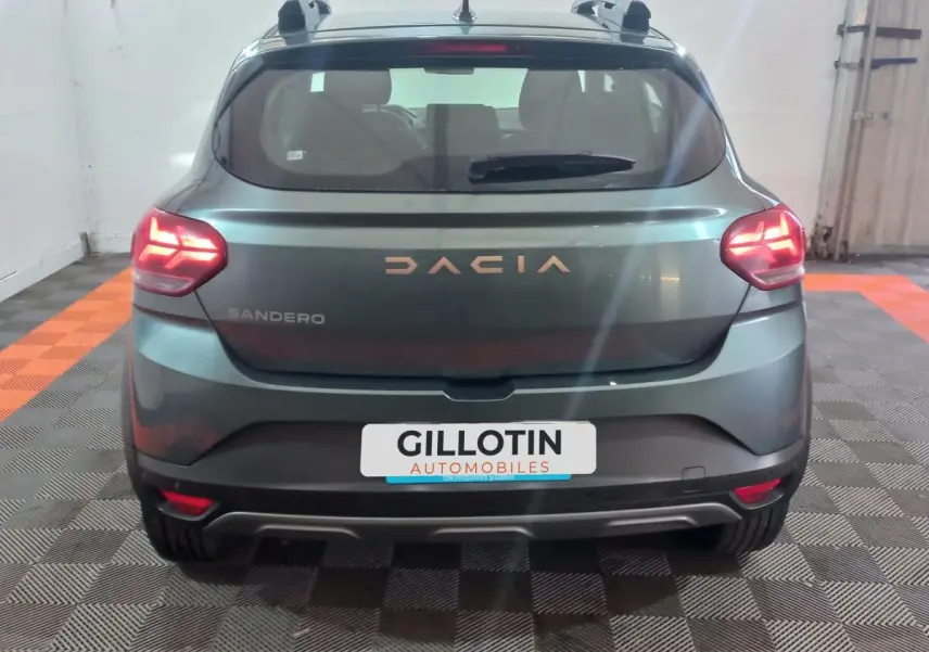 Vue arrière d'une Dacia Sandero Extreme+ TCe 110 2024 vert foncé avec feux LED allumés en intérieur.