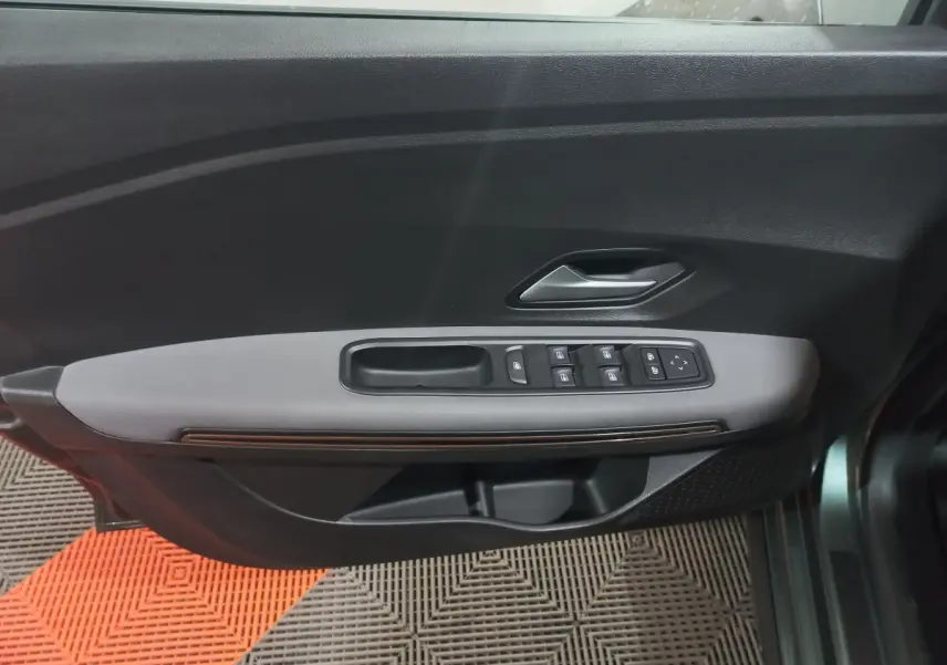Vue rapprochée de la porte avant gauche verte de la Dacia Sandero 2024 avec commandes électriques des vitres et poignée intérieure.