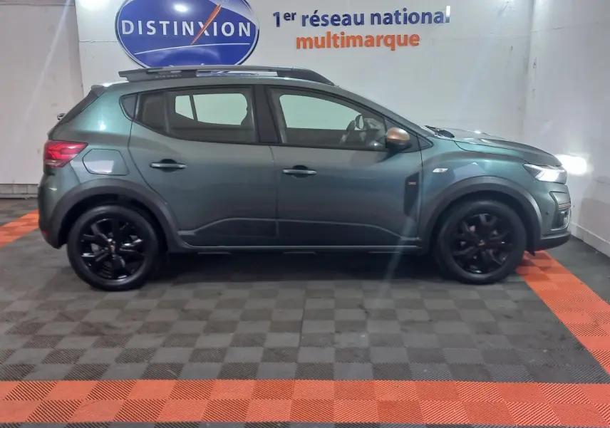 Vue de profil gauche d'une Dacia Sandero Extreme+ TCe 110 2024 vert métallisé avec jantes noires et barres de toit.