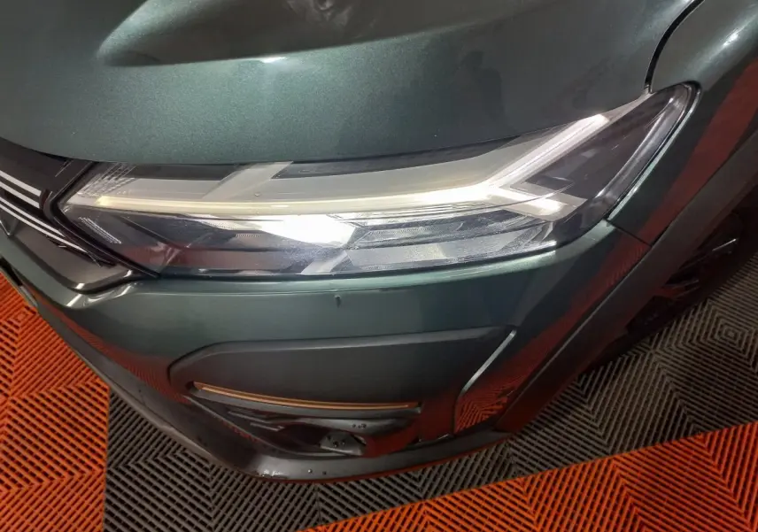 Gros plan sur le phare avant droit vert métallisé de la Dacia Sandero Extreme+ 2024 avec détails LED et pare-chocs noir.