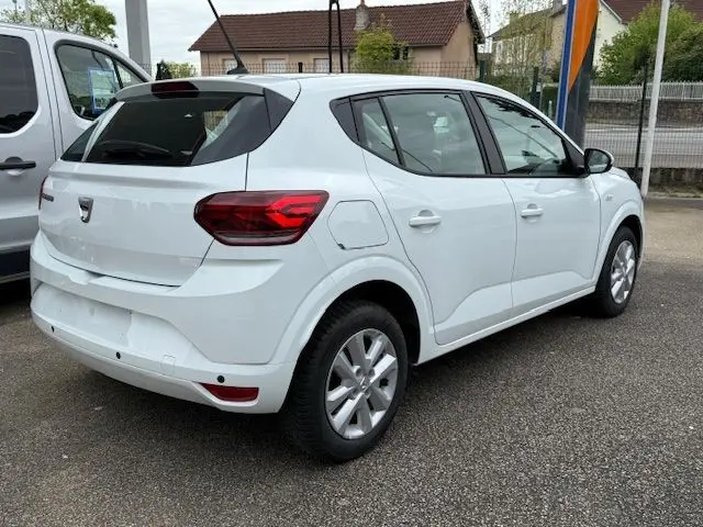 Vue 3/4 arrière droite d'une Dacia Sandero blanche Glacier 2023 avec feux arrière rouges et jantes argentées.
