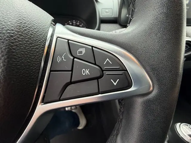 Gros plan sur les commandes au volant côté gauche du Dacia Sandero blanc glacier 2023, boutons multifonctions visibles.