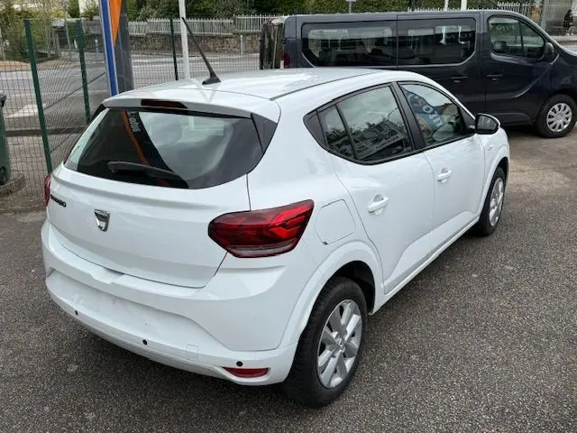 Vue 3/4 arrière droite d'une Dacia Sandero blanche glacier 2023, compacte avec feux arrière rouges et antenne sur le toit.