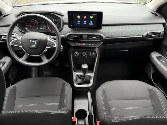Vue intérieure avant du tableau de bord et console centrale du Dacia Sandero 2023 avec volant, écran tactile et boîte manuelle.