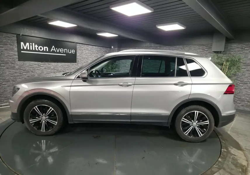 Volkswagen Tiguan gris en profil droit, avec jantes alliage noires et chrome, dans un showroom intérieur.