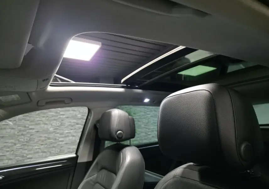 Intérieur du Volkswagen Tiguan 2016, vue sur les sièges avant en cuir noir et toit ouvrant panoramique ouvert.