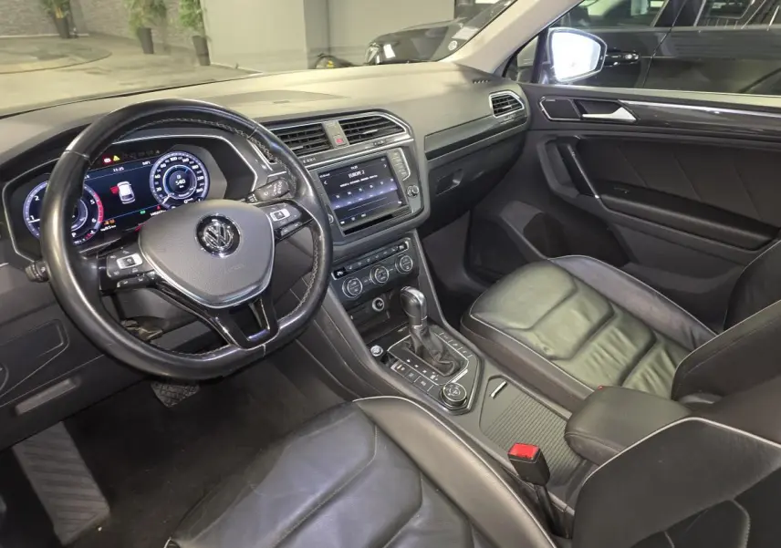 Vue intérieure du Volkswagen Tiguan 2016 côté conducteur, avec tableau de bord numérique et sièges sport cuir noirs.