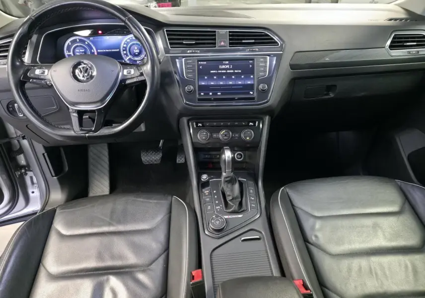 Vue intérieure avant du Volkswagen Tiguan 2016 avec tableau de bord noir, volant cuir multifonctions et console centrale avec écran tactile.