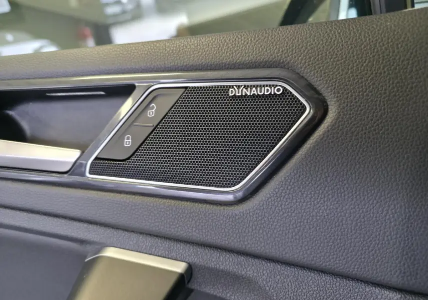 Gros plan sur l'enceinte Dynaudio intégrée à la porte intérieure en simili-cuir noir du Volkswagen Tiguan gris.