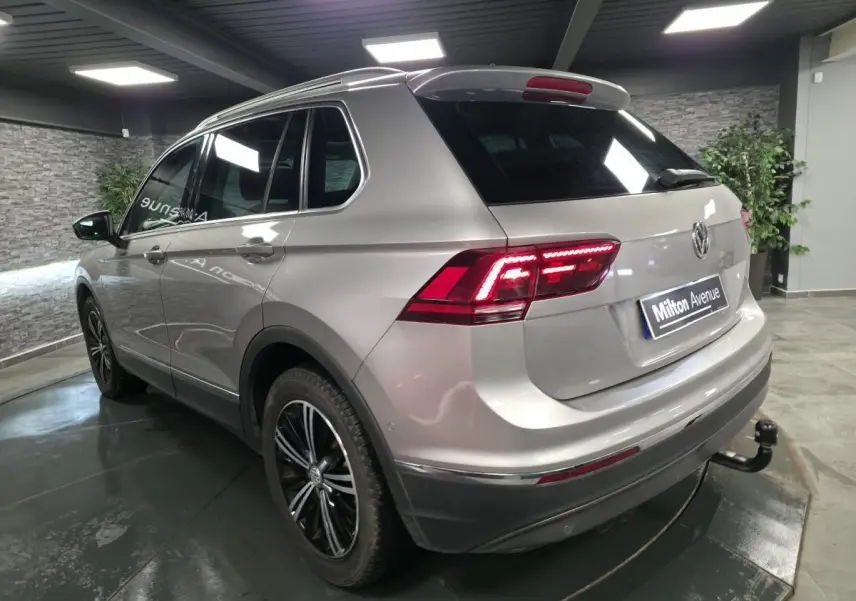Vue 3/4 arrière droit d'un Volkswagen Tiguan gris métallisé avec jantes alliage noires et crochet d'attelage démontable.