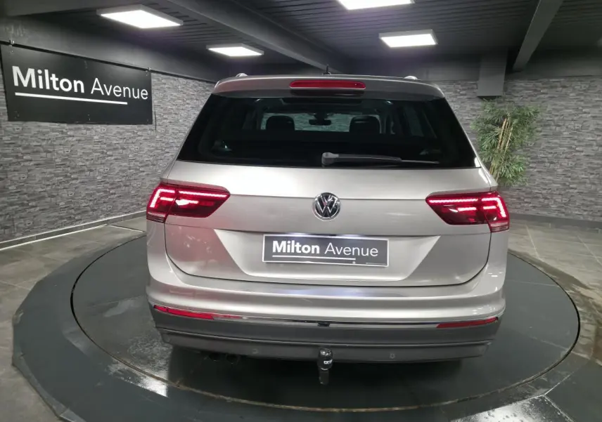 Vue arrière d'un Volkswagen Tiguan gris métallisé avec feux LED allumés et crochet d'attelage visible en intérieur showroom.
