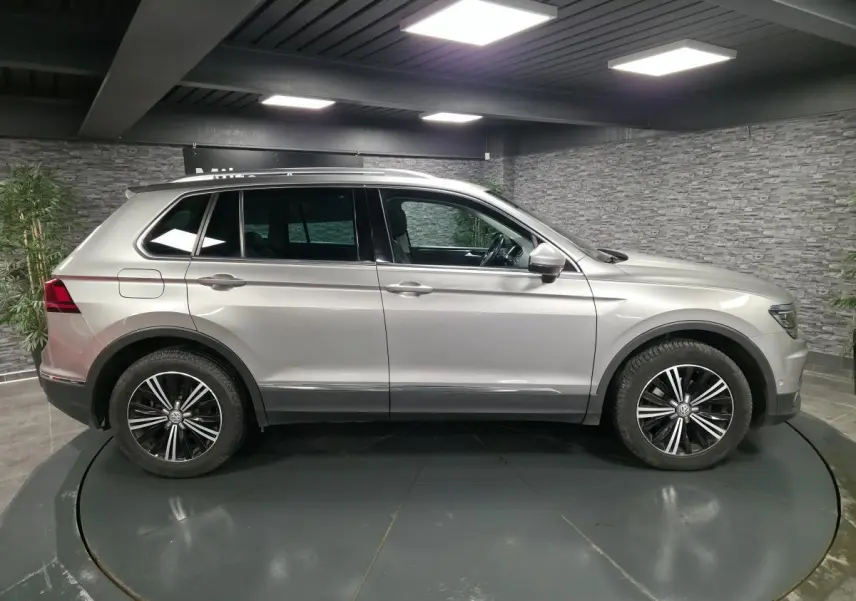 Volkswagen Tiguan gris métallisé vu de profil côté gauche avec jantes alliage noires et toit ouvrant panoramique.