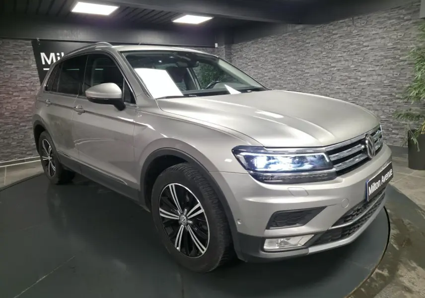 Volkswagen Tiguan gris métallisé vu en 3/4 avant droit avec phares allumés et jantes alliage noires.