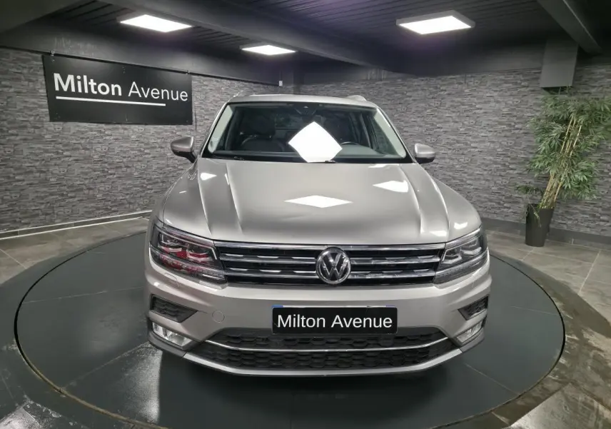 Vue frontale d'un Volkswagen Tiguan gris métallisé dans un showroom avec éclairage intérieur et panneau Milton Avenue.