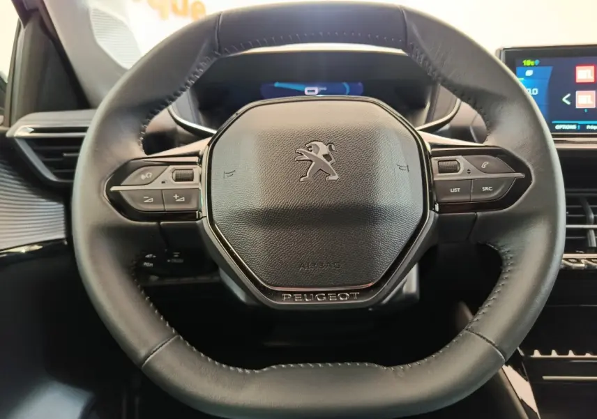 Gros plan sur le volant cuir noir multifonctions de la Peugeot 208 électrique avec tableau de bord numérique en arrière-plan.