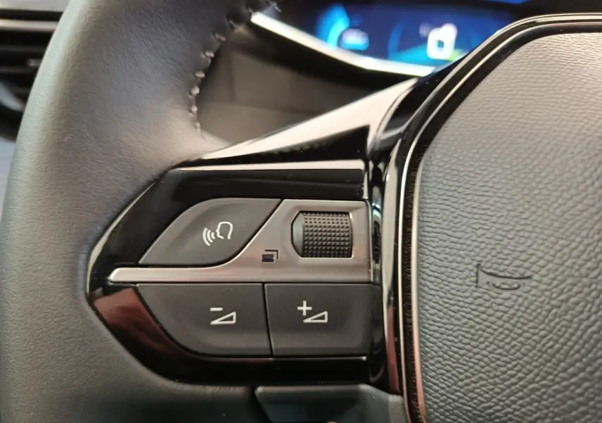 Gros plan sur les commandes vocales et volume au volant cuir noir de la Peugeot 208 électrique gris clair 2022.