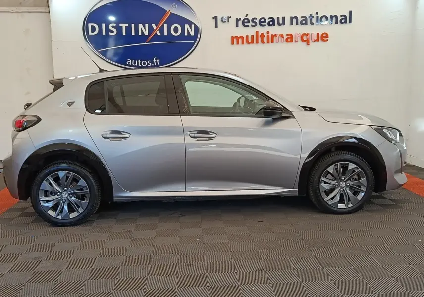 Vue de profil droit d'une Peugeot 208 Electrique ROADTRIP gris clair, avec jantes alliage et protections noires sur les passages de roues.