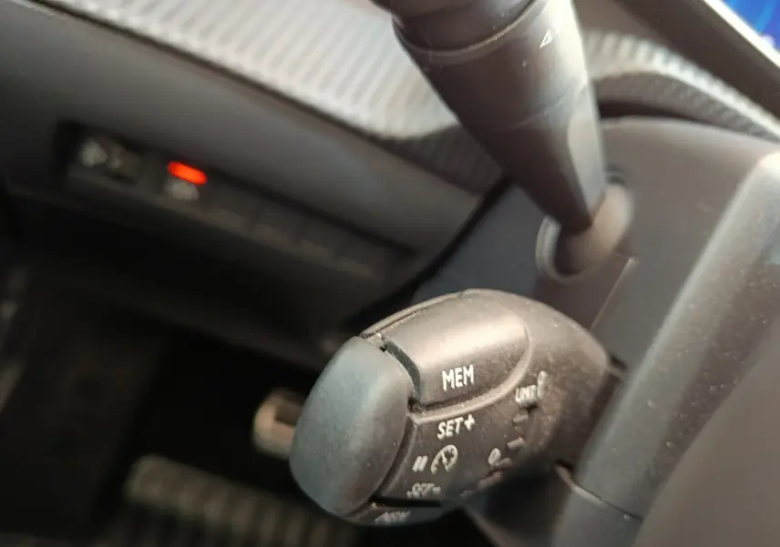 Gros plan sur la commande de régulateur de vitesse noire dans l’habitacle d’une Peugeot 208 électrique gris clair.