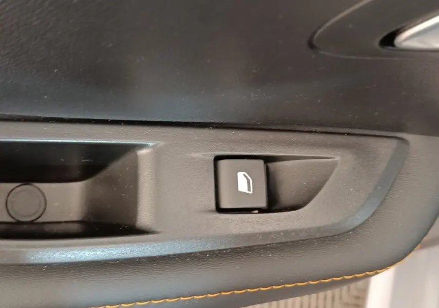 Gros plan sur le bouton de commande de la vitre, intérieur noir avec surpiqûres orange, Peugeot 208 électrique gris clair.