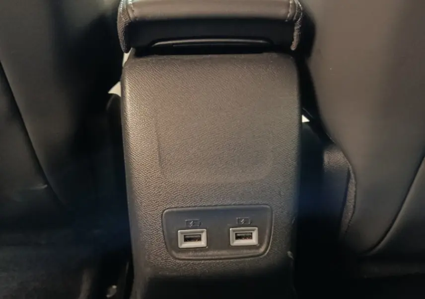 Vue rapprochée de la console centrale arrière noire avec deux ports USB dans l’habitacle d’une Peugeot 208 électrique gris clair.
