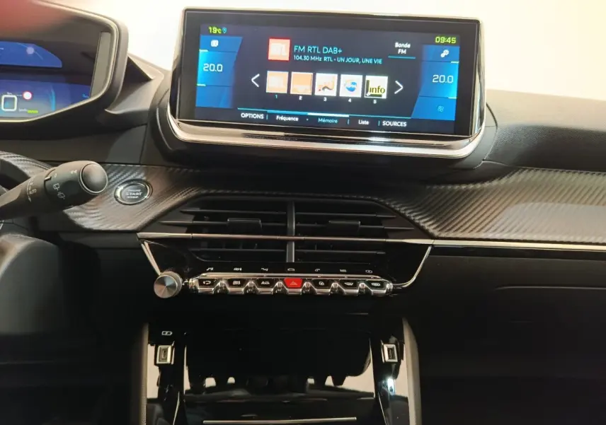 Vue intérieure centrée sur le tableau de bord noir avec écran tactile 10 pouces et commandes piano du Peugeot 208 électrique gris clair.