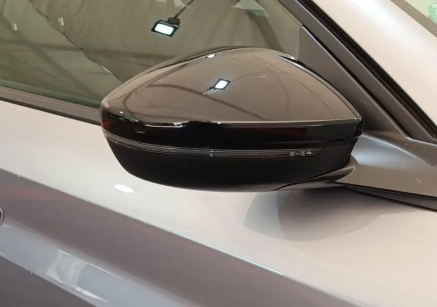 Rétroviseur noir côté gauche sur Peugeot 208 électrique gris clair, vue rapprochée en intérieur.