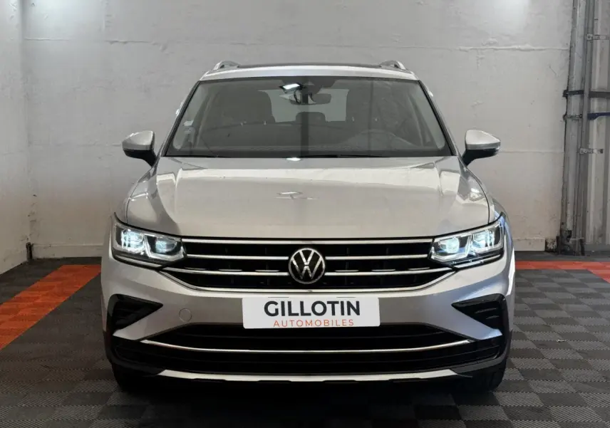 Vue avant d'un Volkswagen Tiguan gris clair avec phares LED allumés et calandre chromée dans un garage.