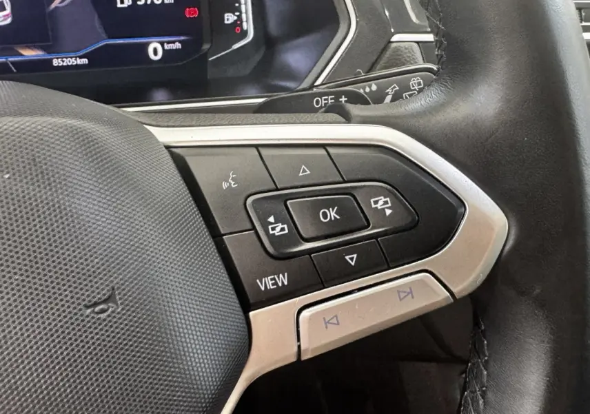 Gros plan sur les commandes multifonctions à droite du volant cuir noir du Volkswagen Tiguan gris clair, tableau de bord digital en arrière-plan.