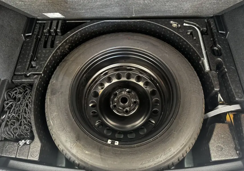 Vue plongeante sur la roue de secours noire et les outils dans le coffre du Volkswagen Tiguan gris clair 2021.