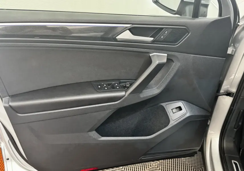 Vue rapprochée de la porte avant gauche gris clair du Volkswagen Tiguan 2021 avec commandes de vitres et poignée argentée.