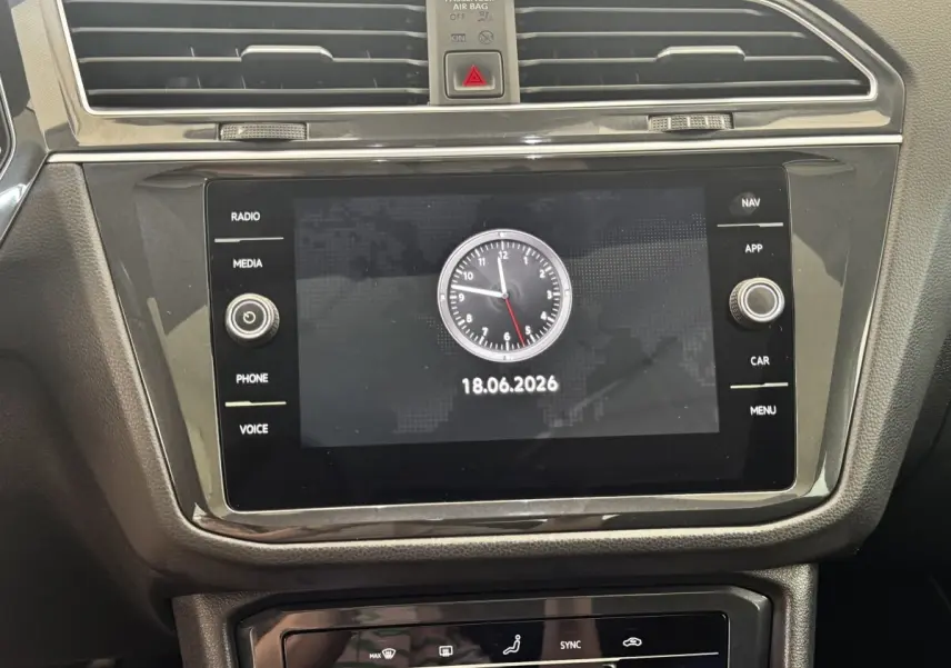 Gros plan sur l’écran tactile central noir du tableau de bord du Volkswagen Tiguan avec horloge digitale affichée.
