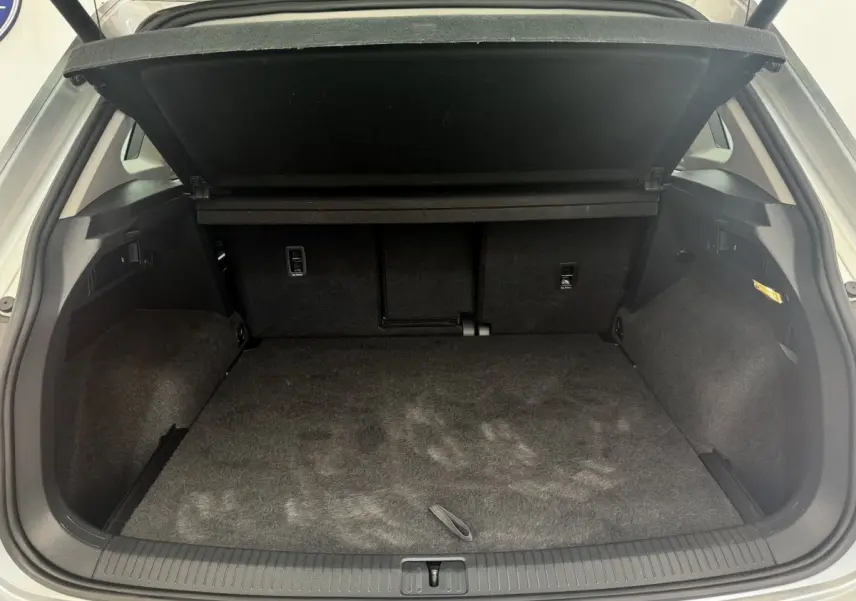 Coffre ouvert vu de l'arrière d'un Volkswagen Tiguan gris clair, espace de chargement propre et tapis noir.