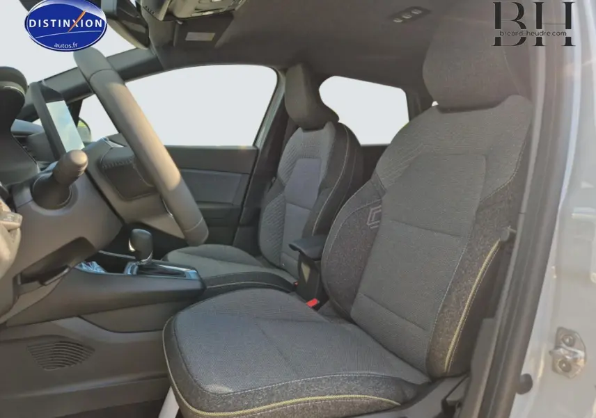 Vue intérieure côté gauche sur les sièges avant gris du Renault Captur 1.6 E-Tech hybride 2025, volant et console visibles.